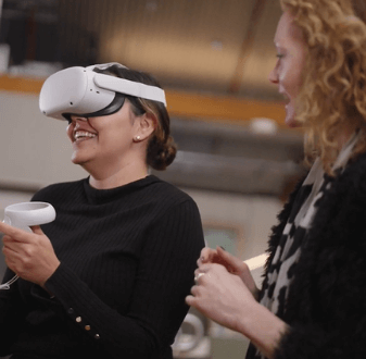 Person wearing virtual reality (VR) headset and holding controller, while another person watches. Torrens University wins Catalyst Award for virtual fashion studio.