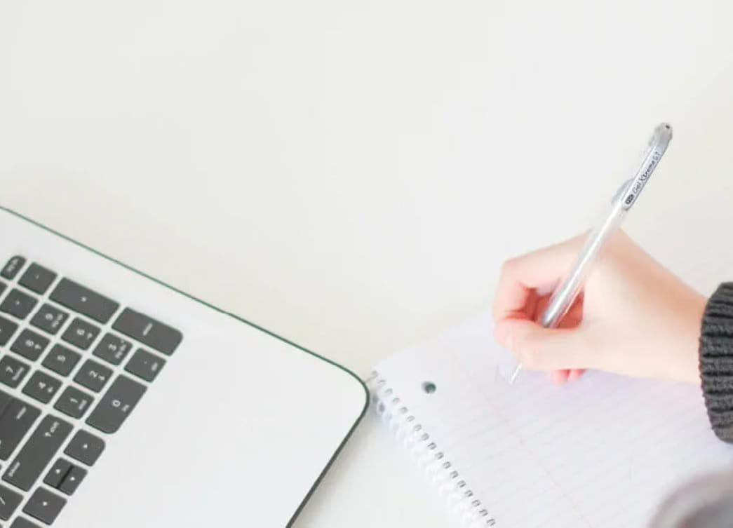 Woman writing on notepad next to a laptop